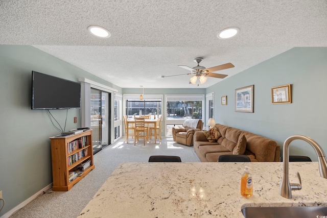 carpeted living area featuring a textured ceiling, ceiling fan, a sink, and baseboards