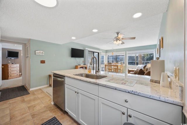 kitchen featuring light stone counters, stainless steel dishwasher, white cabinetry, a sink, and a textured ceiling