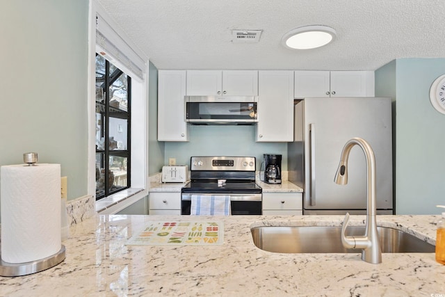 kitchen with visible vents, white cabinets, appliances with stainless steel finishes, light stone countertops, and a sink