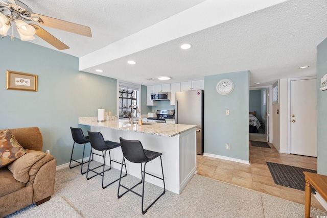 kitchen featuring a textured ceiling, light stone counters, a breakfast bar area, a peninsula, and appliances with stainless steel finishes