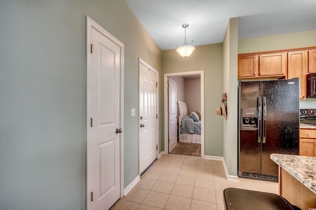 kitchen featuring light tile patterned floors, baseboards, light stone countertops, black appliances, and pendant lighting