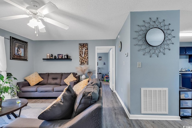 living room featuring baseboards, visible vents, ceiling fan, wood finished floors, and a textured ceiling