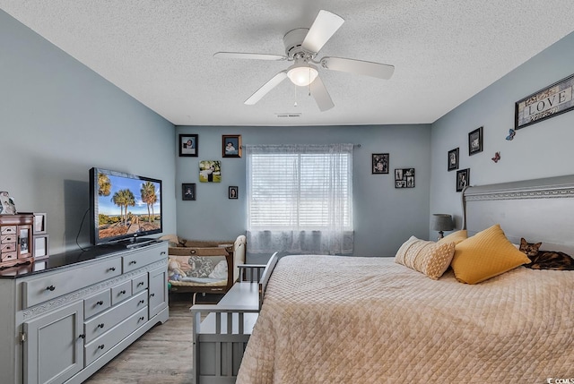 bedroom with a textured ceiling, visible vents, light wood-style flooring, and a ceiling fan