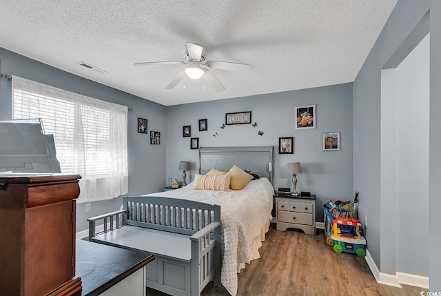 bedroom with baseboards, visible vents, a ceiling fan, wood finished floors, and a textured ceiling