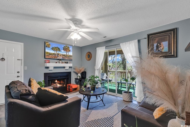 living area featuring a ceiling fan, a warm lit fireplace, visible vents, and a textured ceiling