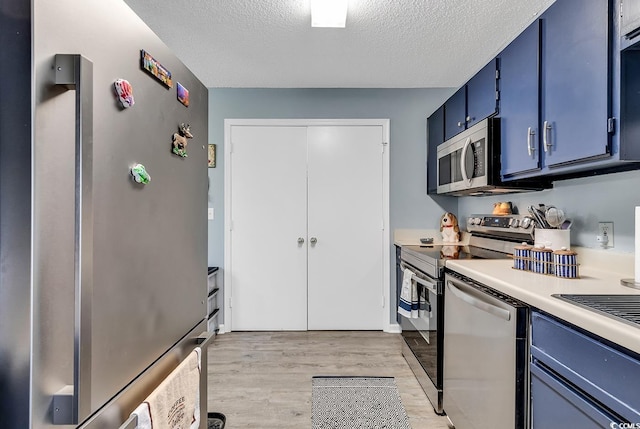 kitchen featuring a textured ceiling, light countertops, appliances with stainless steel finishes, blue cabinetry, and light wood-type flooring