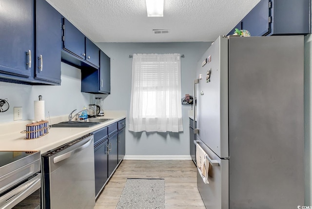 kitchen with light wood-style flooring, stainless steel appliances, a sink, visible vents, and blue cabinetry