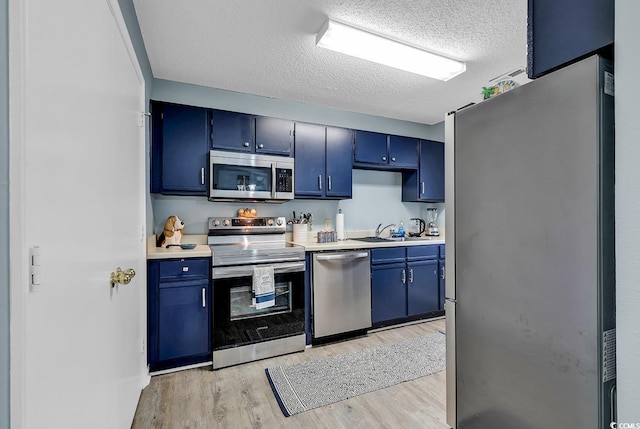 kitchen featuring blue cabinetry, stainless steel appliances, light countertops, a sink, and light wood-type flooring