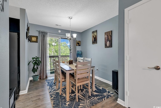 dining area featuring a chandelier, a textured ceiling, wood finished floors, and visible vents