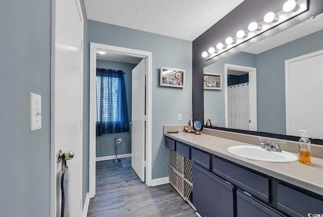 full bathroom with a textured ceiling, wood finished floors, a sink, baseboards, and double vanity