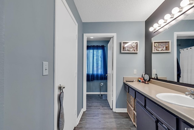 full bathroom with a textured ceiling, wood finished floors, vanity, and baseboards