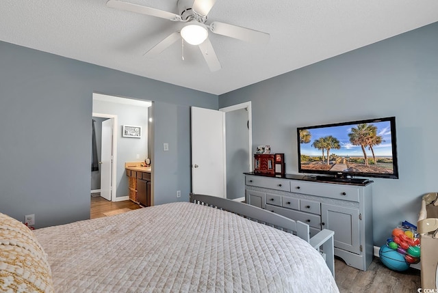 bedroom featuring baseboards, connected bathroom, a ceiling fan, wood finished floors, and a textured ceiling