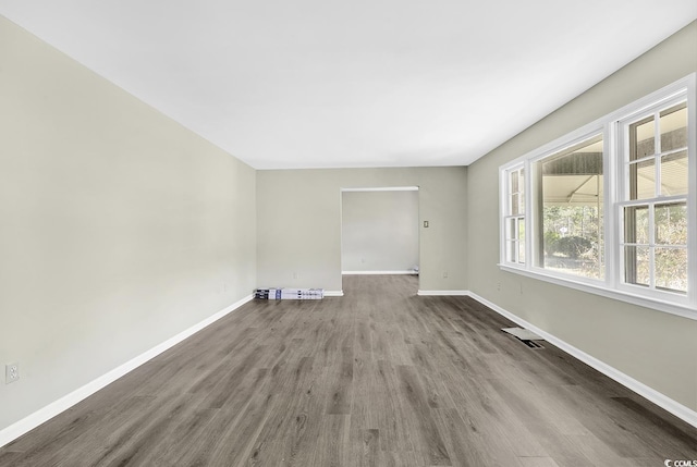 empty room with wood finished floors, visible vents, and baseboards