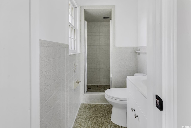 bathroom featuring toilet, a stall shower, wainscoting, and tile walls