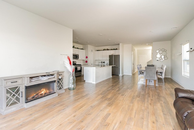 living area featuring a glass covered fireplace, baseboards, and light wood-style floors