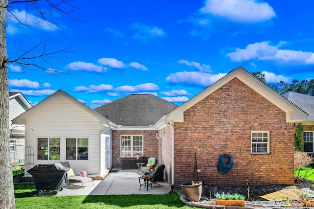 rear view of house featuring a shingled roof, a lawn, a patio, and brick siding