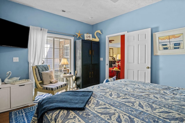 bedroom featuring a ceiling fan, visible vents, a textured ceiling, and wood finished floors