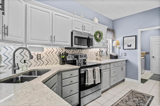 kitchen with white cabinets, a sink, stainless steel appliances, gray cabinetry, and backsplash