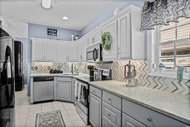 kitchen with light tile patterned floors, gray cabinetry, white cabinetry, appliances with stainless steel finishes, and decorative backsplash