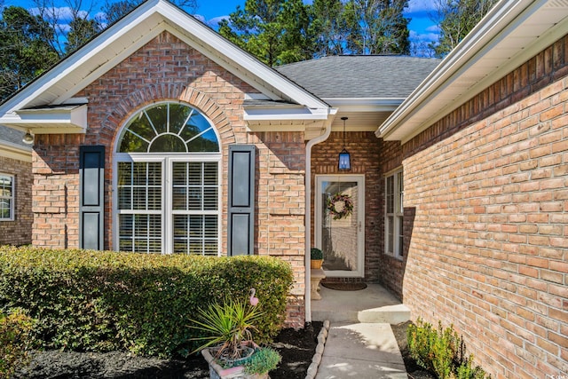 property entrance featuring brick siding and roof with shingles