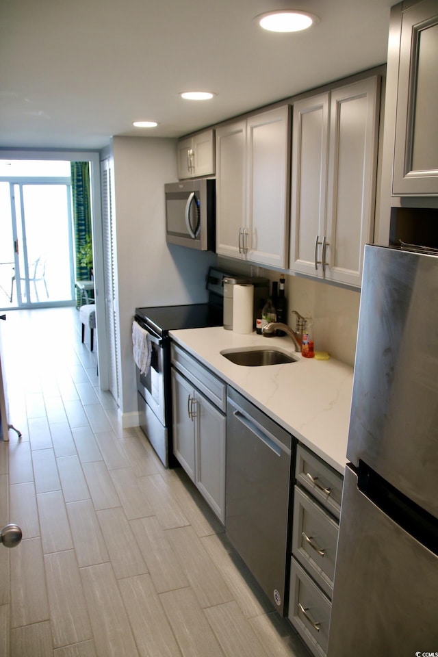 kitchen with light stone counters, stainless steel appliances, gray cabinetry, expansive windows, and a sink