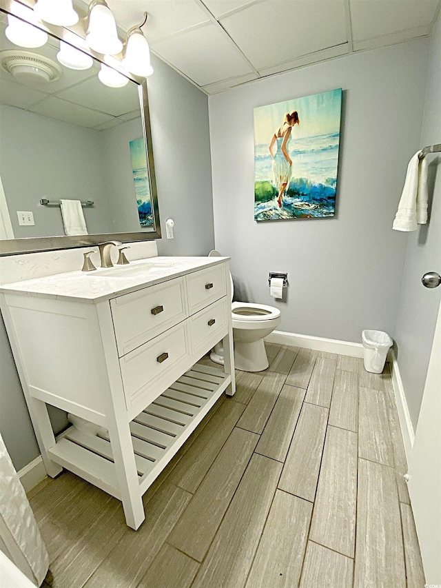 bathroom with a paneled ceiling, toilet, vanity, baseboards, and wood tiled floor