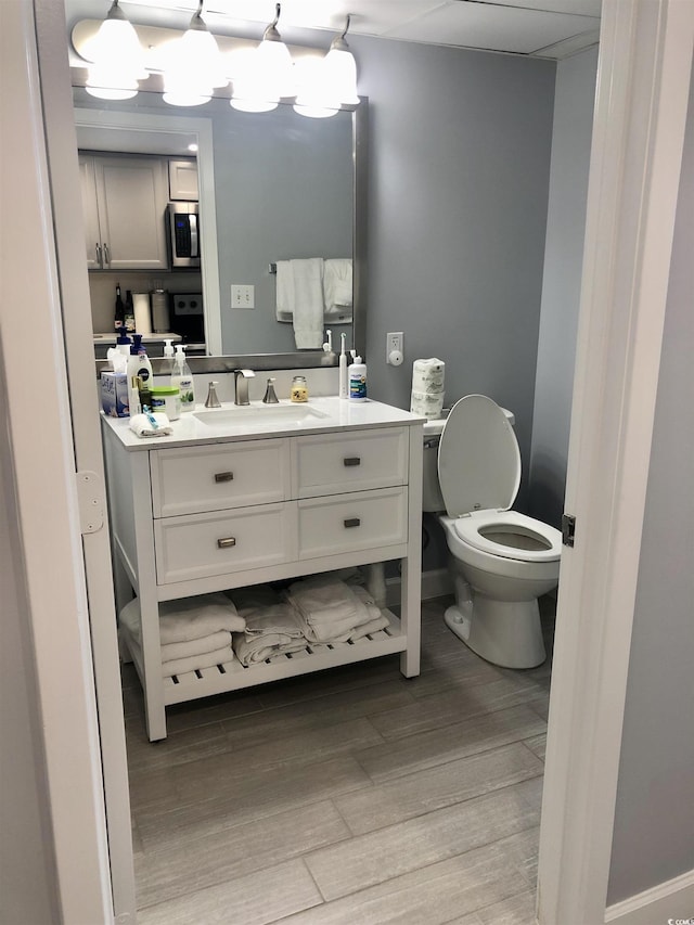 bathroom featuring toilet, a notable chandelier, wood finished floors, vanity, and baseboards