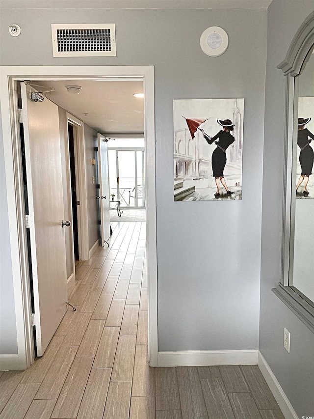 hallway featuring baseboards, visible vents, and wood finish floors