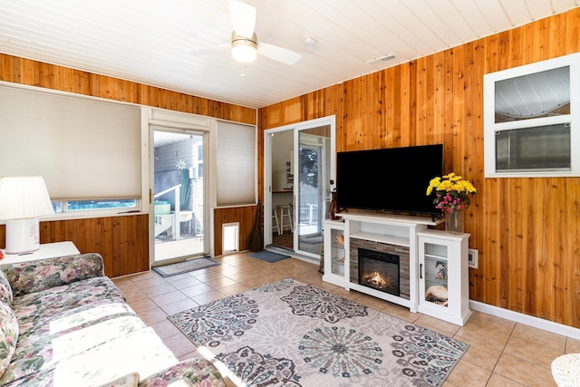 tiled living room featuring a ceiling fan, a glass covered fireplace, visible vents, and wooden walls