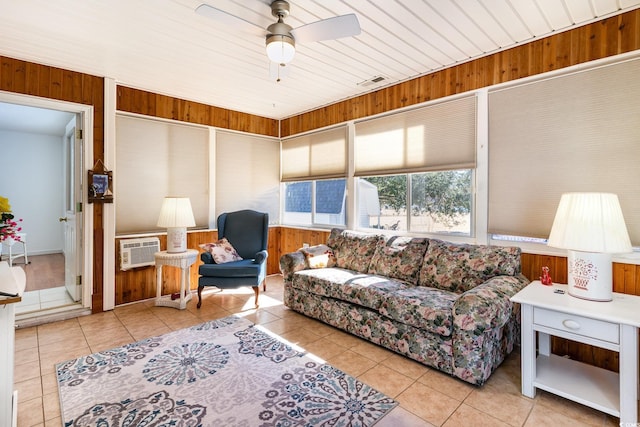 tiled living area with wood walls, a wall mounted air conditioner, visible vents, and a ceiling fan