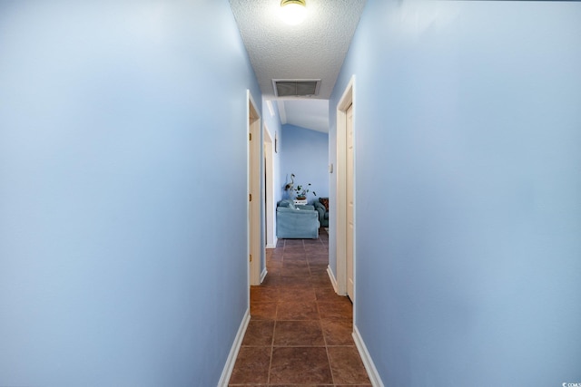 hallway with a textured ceiling, dark tile patterned flooring, visible vents, and baseboards