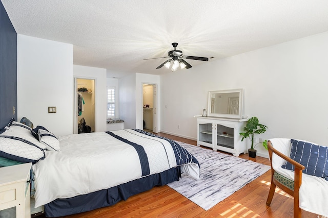 bedroom with a closet, a spacious closet, a ceiling fan, a textured ceiling, and wood finished floors