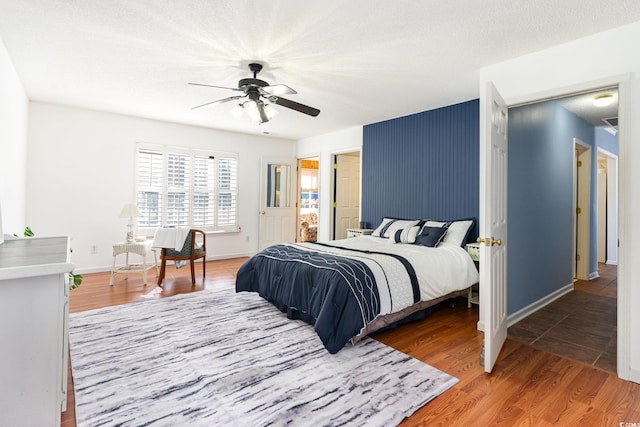 bedroom featuring baseboards, ceiling fan, a textured ceiling, and light wood finished floors