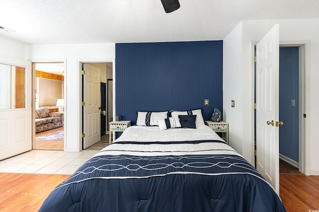 bedroom featuring a textured ceiling, an accent wall, wood finished floors, visible vents, and a ceiling fan