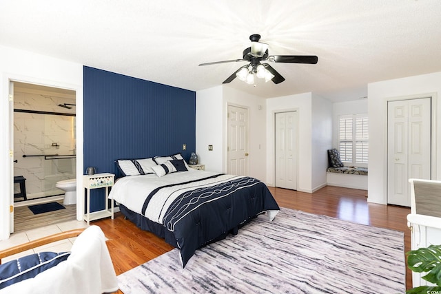 bedroom with multiple closets, a ceiling fan, ensuite bath, and wood finished floors