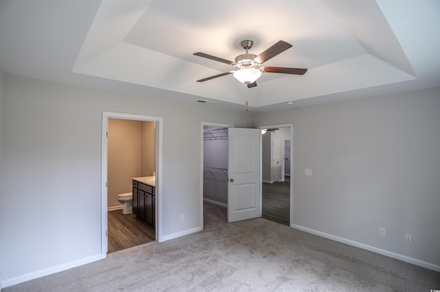 unfurnished bedroom with carpet floors, a tray ceiling, a walk in closet, and a closet