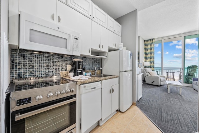 kitchen with white appliances, a sink, white cabinetry, backsplash, and a wall of windows