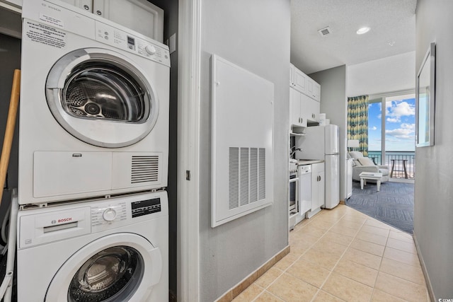 laundry area featuring light tile patterned floors, laundry area, baseboards, a textured ceiling, and stacked washing maching and dryer