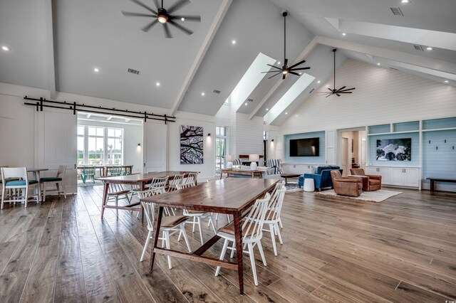 dining room with ceiling fan, high vaulted ceiling, hardwood / wood-style floors, beam ceiling, and a skylight