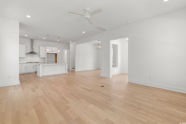 unfurnished living room with ceiling fan, light wood finished floors, baseboards, recessed lighting, and a chandelier