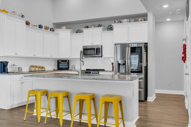 kitchen featuring light stone counters, tasteful backsplash, appliances with stainless steel finishes, white cabinetry, and wood finished floors