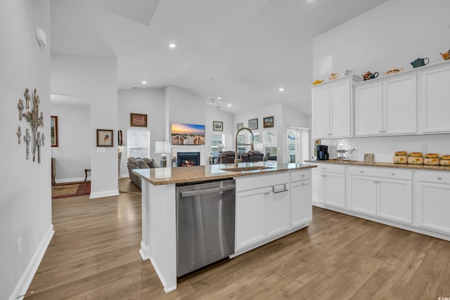 kitchen featuring a warm lit fireplace, a sink, stainless steel dishwasher, light wood-type flooring, and a center island with sink