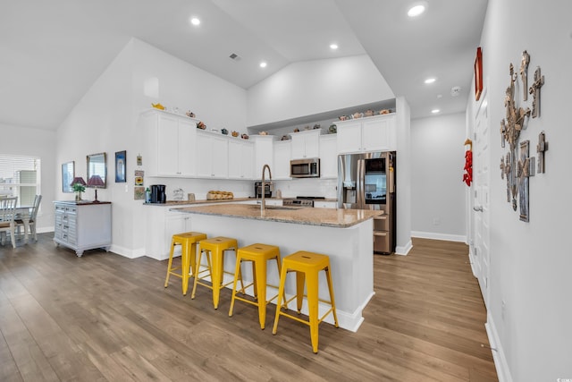 kitchen with a center island with sink, stainless steel appliances, wood finished floors, high vaulted ceiling, and a kitchen bar