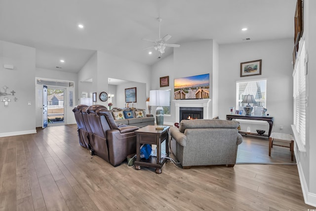 living area featuring ceiling fan, high vaulted ceiling, light wood-style flooring, recessed lighting, and a glass covered fireplace