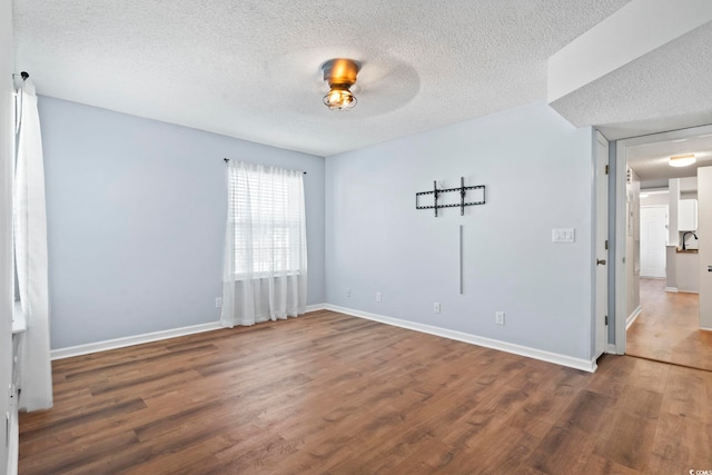 unfurnished room with a textured ceiling, wood finished floors, and baseboards