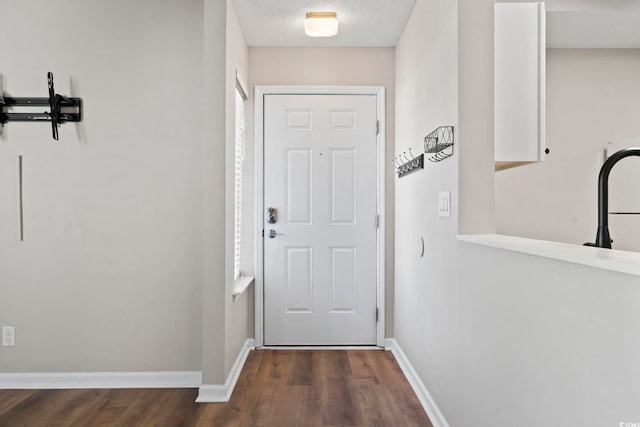 doorway featuring baseboards, dark wood finished floors, and a textured ceiling