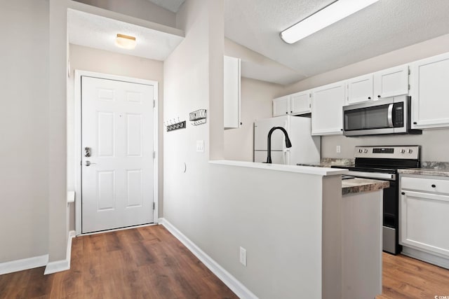 kitchen with appliances with stainless steel finishes, dark wood-type flooring, white cabinetry, a textured ceiling, and baseboards