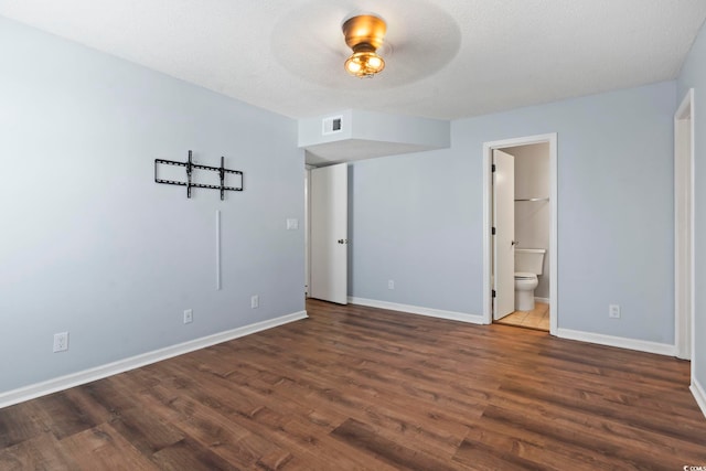 unfurnished bedroom with connected bathroom, a textured ceiling, baseboards, and wood finished floors