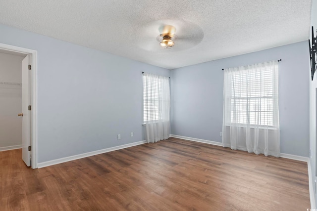 unfurnished room featuring a textured ceiling, baseboards, and wood finished floors