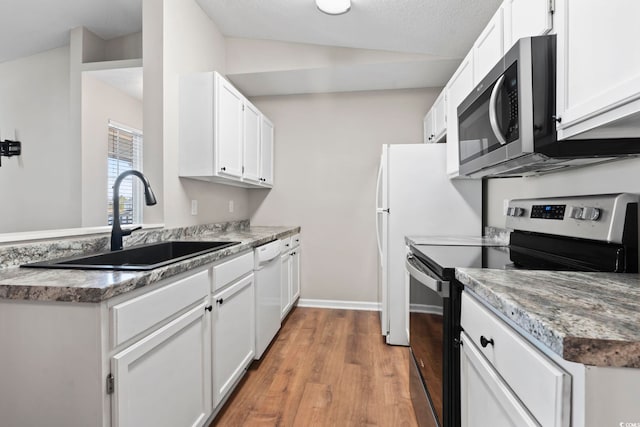 kitchen featuring lofted ceiling, stainless steel appliances, light wood-style floors, white cabinetry, and a sink